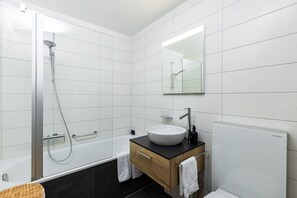Un baño moderno con ducha de vidrio, un lavamanos blanco y un espejo sobre el tocador.