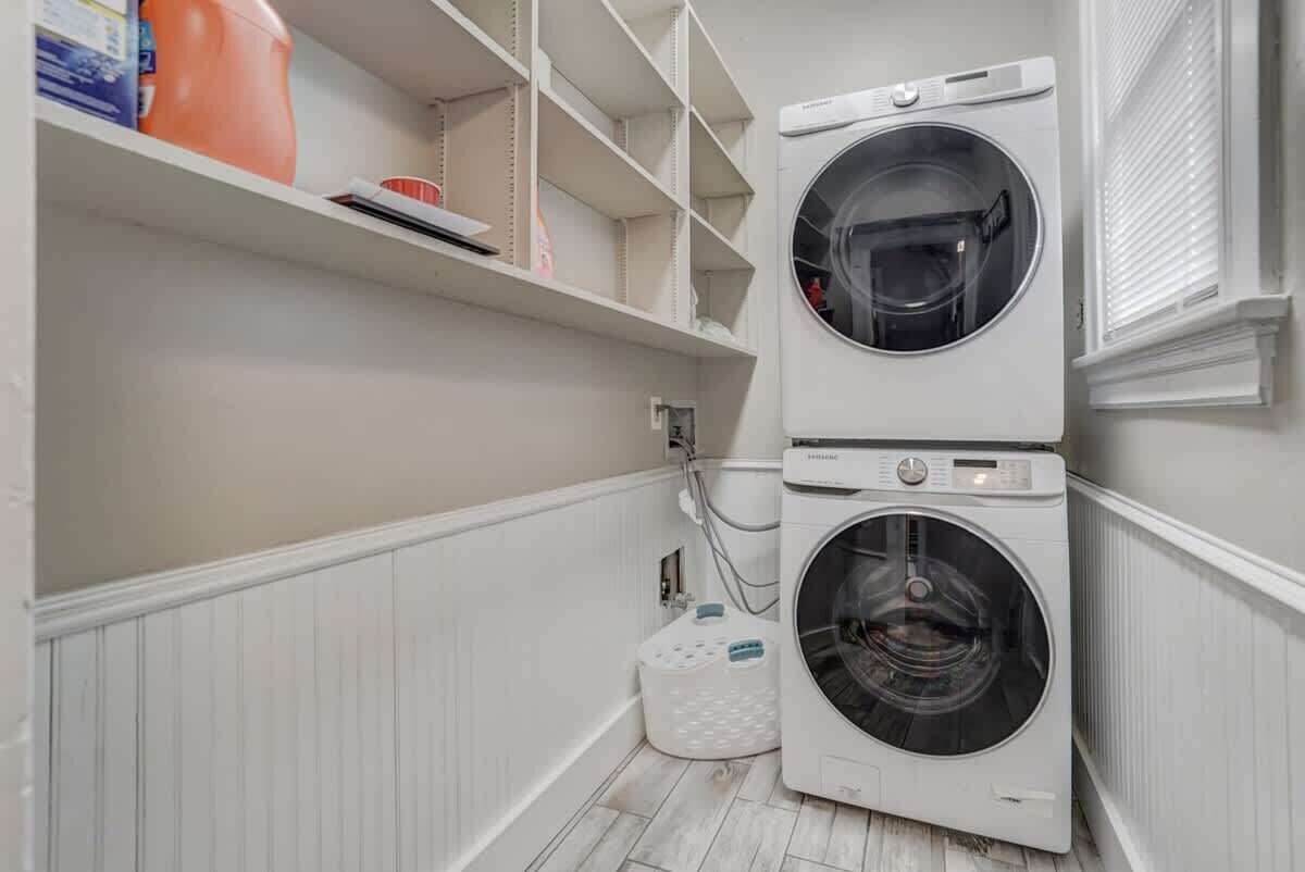 A laundry room with two stacked front-loading washing machines, a shelf with cleaning supplies, and a white storage bin.