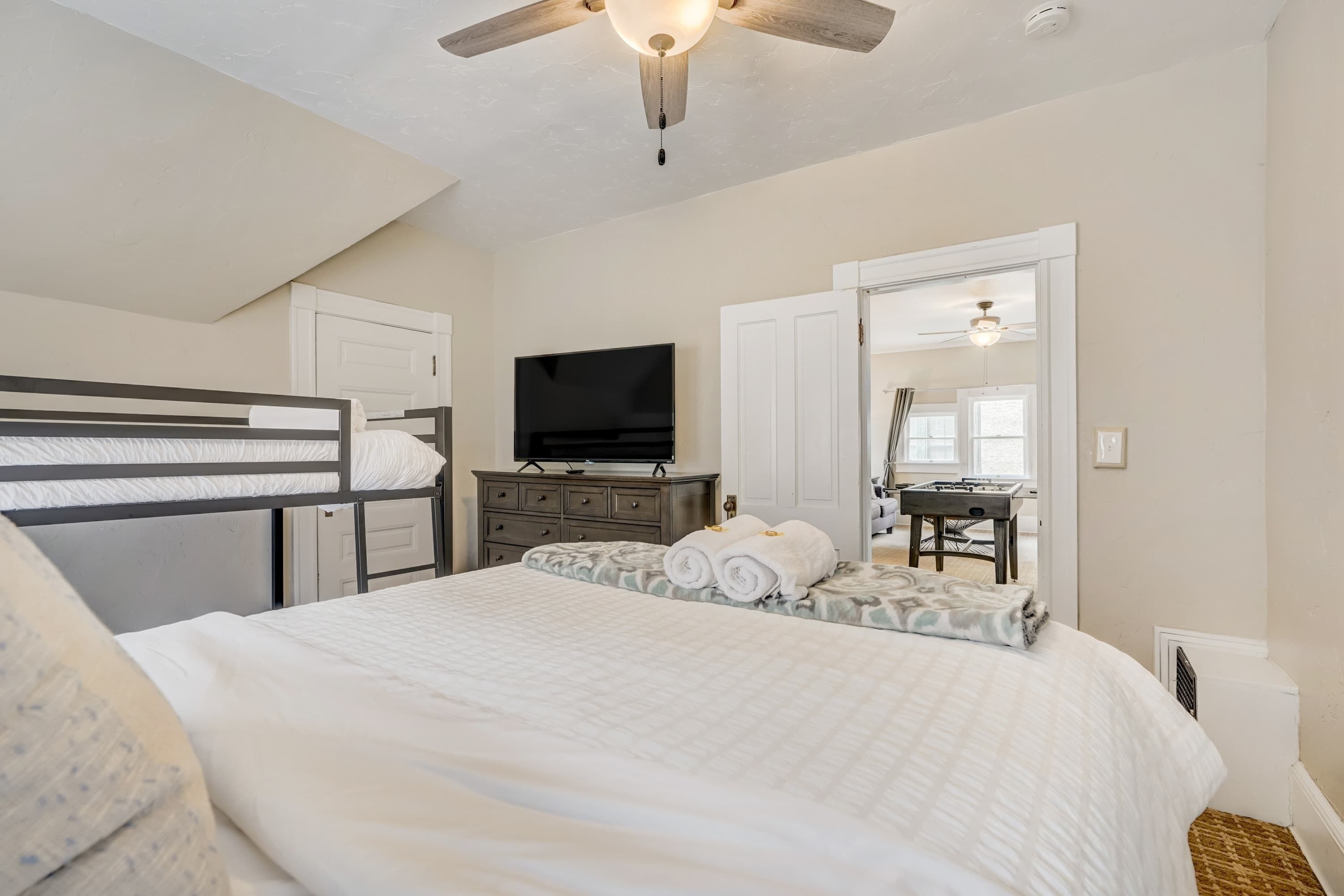 A bedroom with a bunk bed, a flat-screen TV, a dresser, a desk with a mirror, and a ceiling fan.