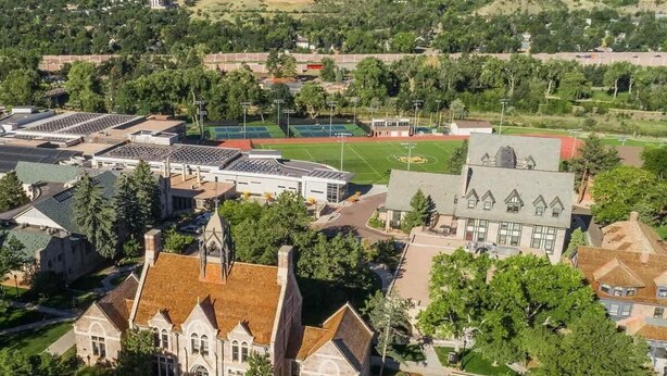 Vista aérea de un campus con un edificio destacado que tiene un techo pronunciado y una amplia entrada principal.