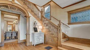 A grand staircase with ornate railings and a chandelier, leading to a dining area with a white console table and a chandelier. - Crescent Estate! Hot Tub, Mtn Views, Walk DT, Golf (Colorado Springs)