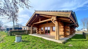 A log cabin with a porch, a table, and chairs. - Unique log house for 6 pers. with terrace and unobstructed view near Wadden Sea (Den Oever)