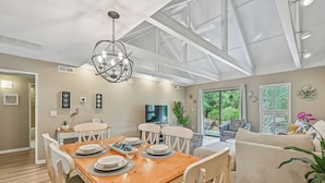 A spacious living area with a wooden dining table, white chairs, and a comfortable sofa.