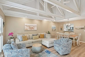 A spacious living room with a sectional sofa, round coffee table, and patterned armchairs. A dining area with a wooden table and chairs is visible in the background. - 501 Queen's Grant ~ Palmetto Dunes Townhome | Walk to Pickleball & Tennis! (Hilton Head Island)