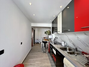 Eine moderne Küche mit Marmorarbeitsplatte, Edelstahlspüle und roten Schränken.