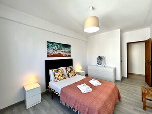 Ein Schlafzimmer mit Bett, Nachttischlampen, einem Nachttisch, einem Schminktisch, einem Spiegel und einer Tür.
