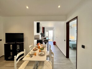 Ein moderner Essbereich mit Tisch für zwei Personen, einem Fernseher und einer Küche im Hintergrund.