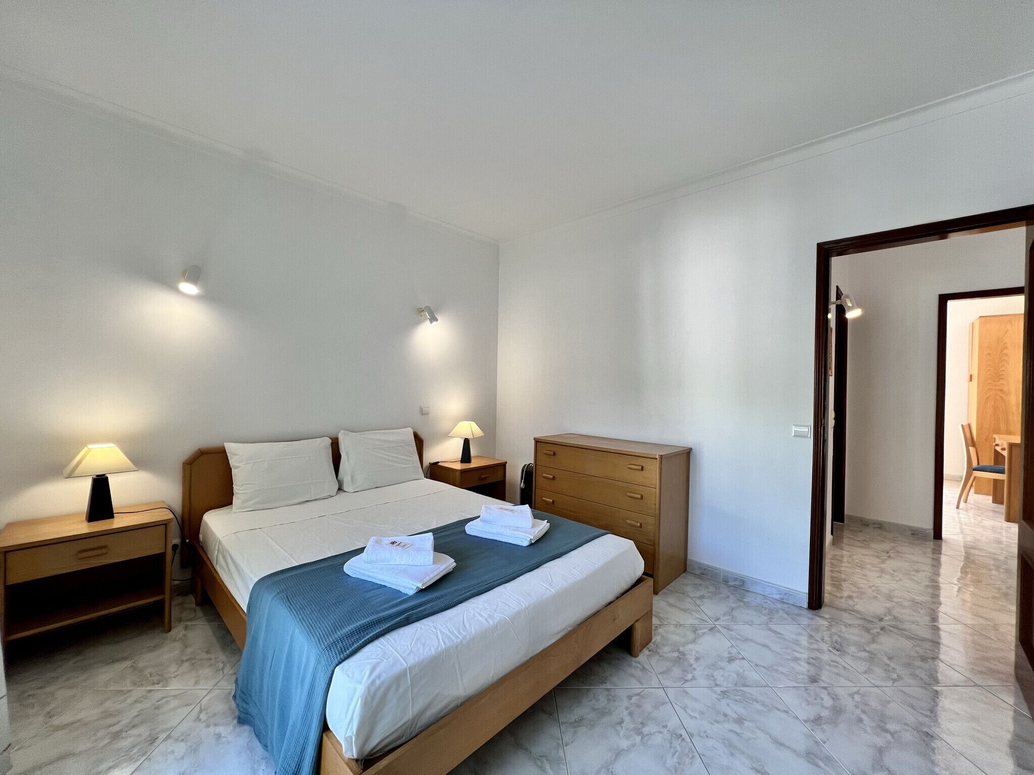 A hotel room with a bed, two bedside tables, a wooden dresser, and a chair in the corner.