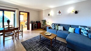 Un salon avec un canapé bleu, une table basse en bois et un coin repas comprenant une table et des chaises.