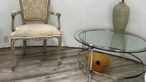 Een stoel met versierde details en een glazen tafel met een gevlochten mand eronder.