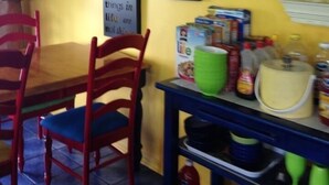 A dining area with a table and chairs, a shelf with kitchen items, and various framed pictures and signs on the walls. - The Blue Water House (Lewes)
