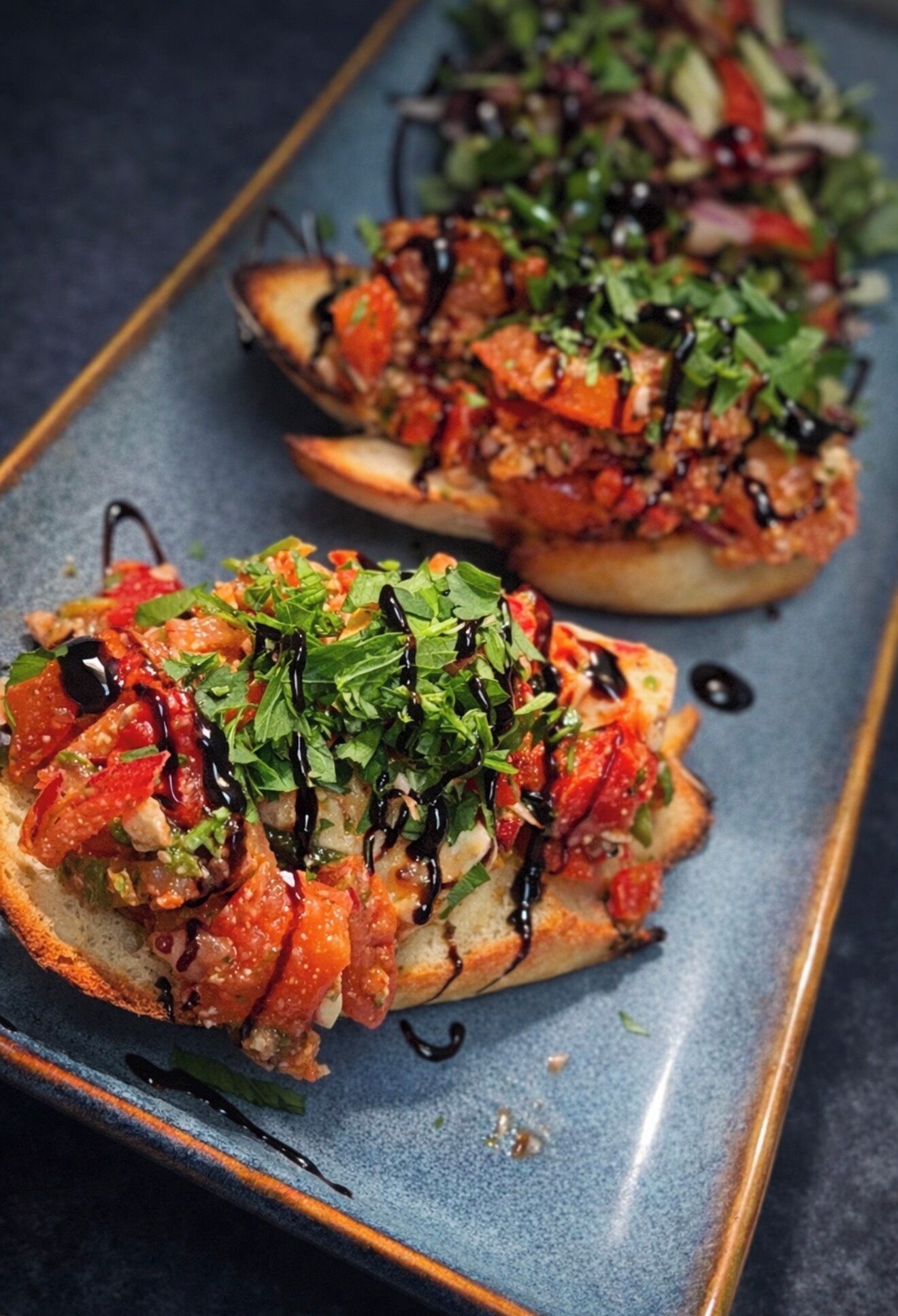 Two open-faced sandwiches with toppings and a drizzle of sauce on a rectangular plate.