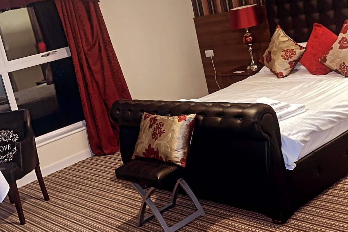 A hotel room with a bed, a chair, a window with curtains, a striped wall, and a ceiling light.