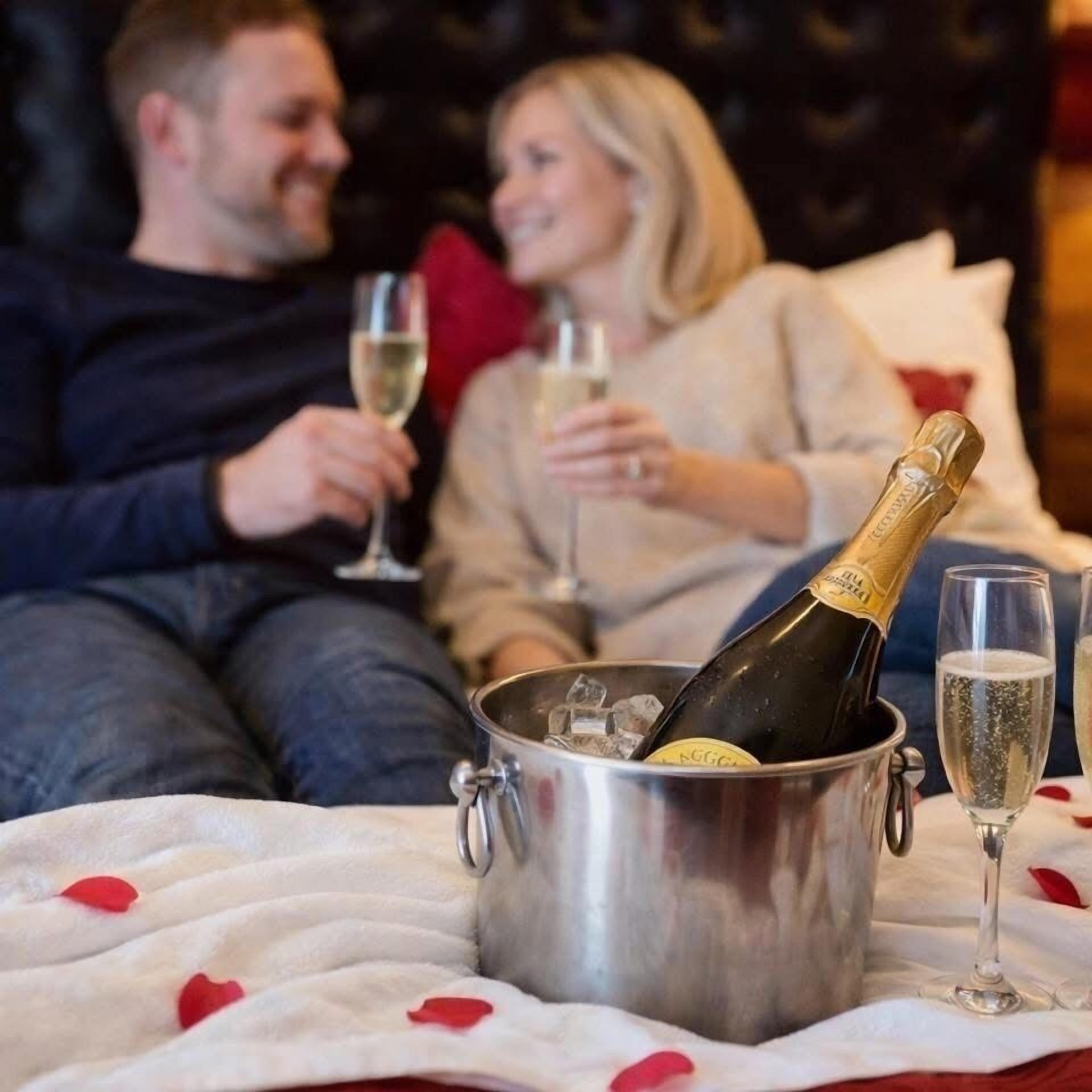 Een koppel zittend op een bed, met een emmer champagne en glazen.