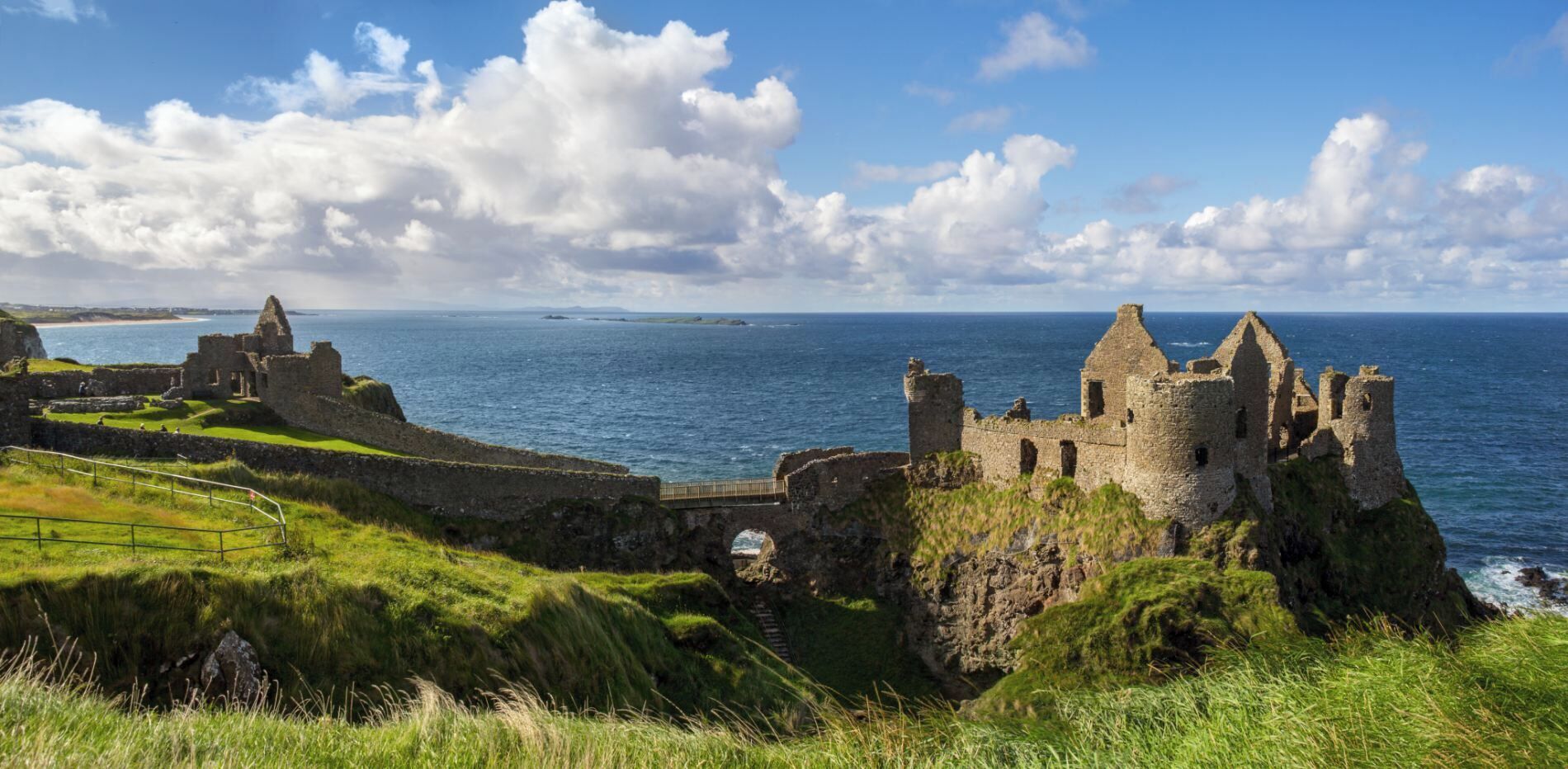 Un castillo de piedra histórico con ruinas, un primer plano de césped y vista al mar.