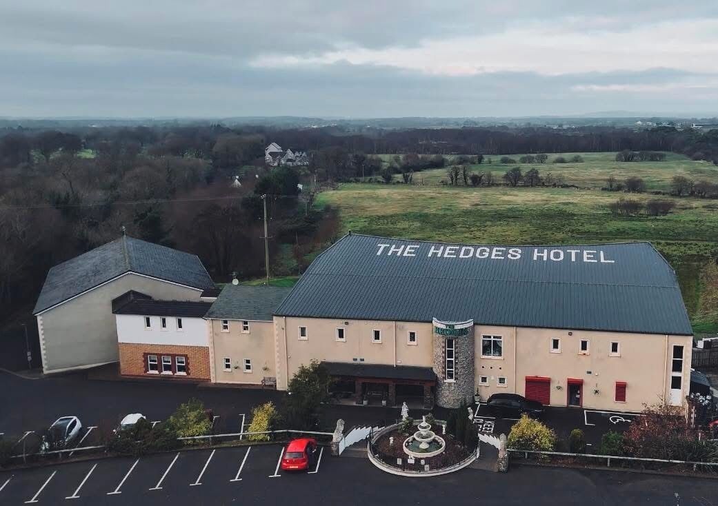 The Hedges Hotel with a large parking lot and a fountain.