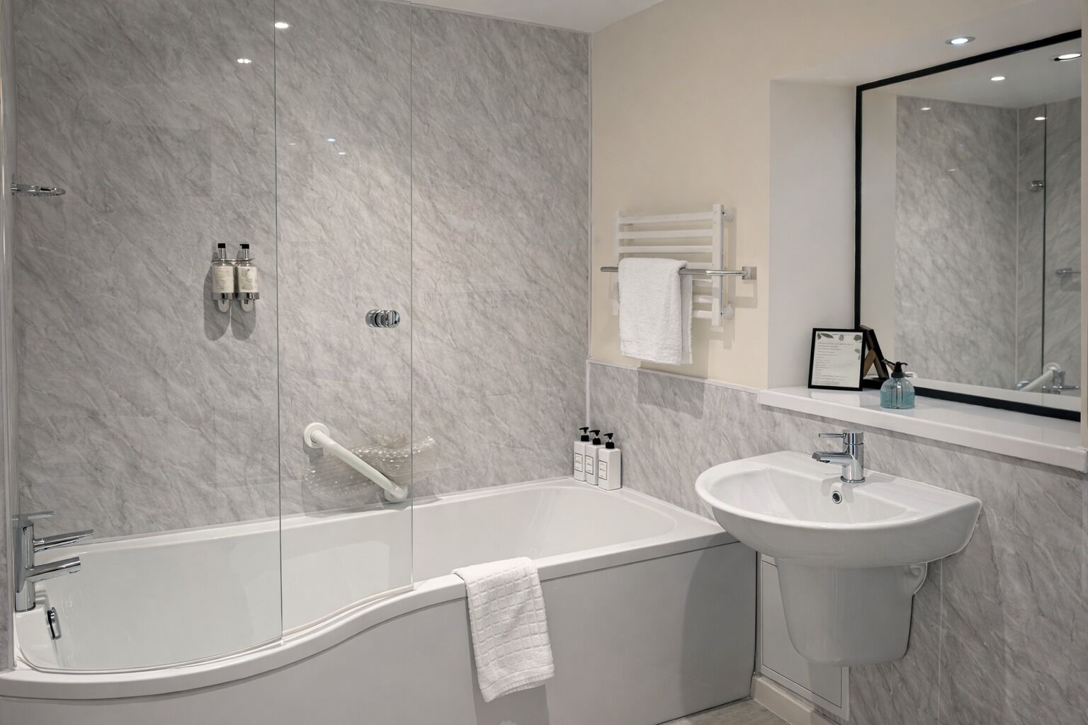 Un baño moderno con una bañera independiente, un lavamanos montado en la pared y un espejo grande.