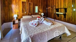 Ein Schlafzimmer mit Holzwandverkleidung, einem großen Bett, zwei Nachttischen, einem Kleiderhaken und einem an der Wand befestigten Regal.