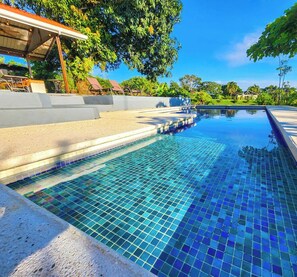 Una piscina con borde de azulejos y una zona de estar cubierta.
