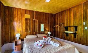 Un dormitorio con paneles de madera, una cama grande, dos mesitas de noche, un perchero y una estantería en la pared.