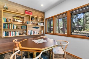 A dining area with a wooden table and chairs, surrounded by bookshelves filled with books and decorative items. - Golfside Oasis with Access to The Cove (Sunriver)