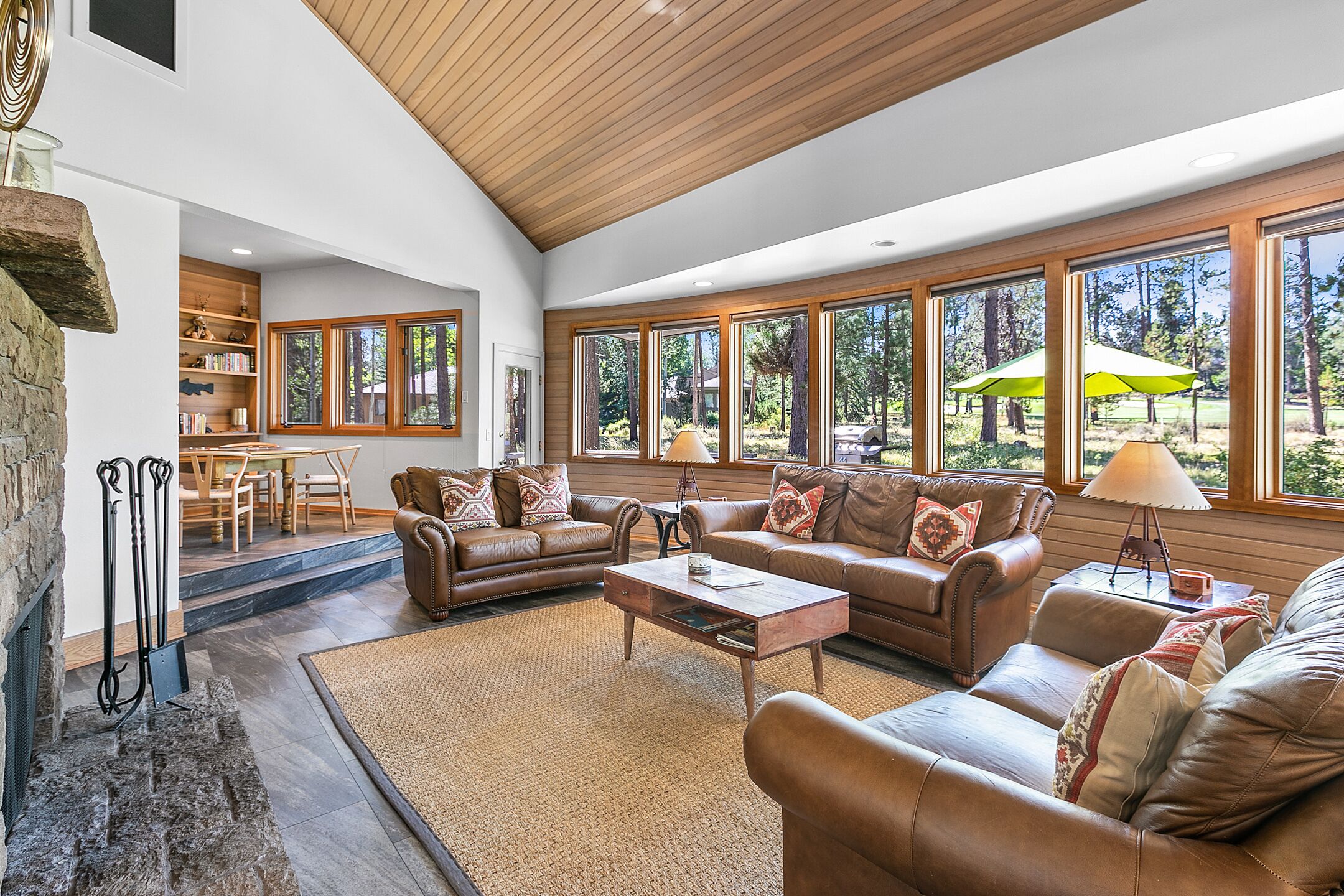 A spacious living room with leather sofas, a fireplace, and large windows offering a view of the outdoors.
