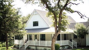 A white two-story house with a porch and a staircase leading to the entrance. - The Lucky Penny Farmhouse on the LBJ Grasslands (Alvord)