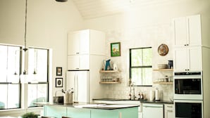 Una cocina con armarios blancos, una isla central, luces colgantes y un ventanal que proporciona luz natural.