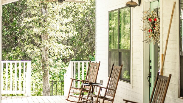 A wooden porch with rocking chairs, a ceiling fan, and a white exterior wall. - The Lucky Penny Farmhouse on the LBJ Grasslands (Alvord)