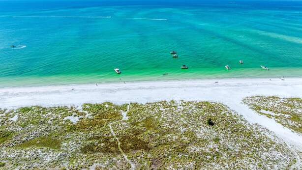 Vista aérea de una playa con aguas turquesas cristalinas, varios barcos y una orilla arenosa.