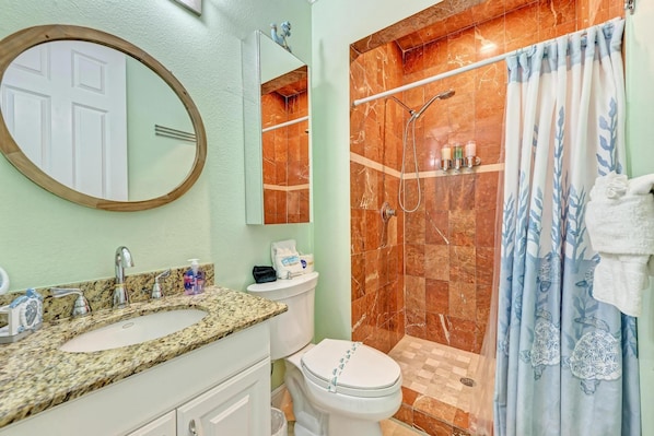 A bathroom with a granite countertop sink, a toilet, a shower with a glass door, and a mirror with a wooden frame.