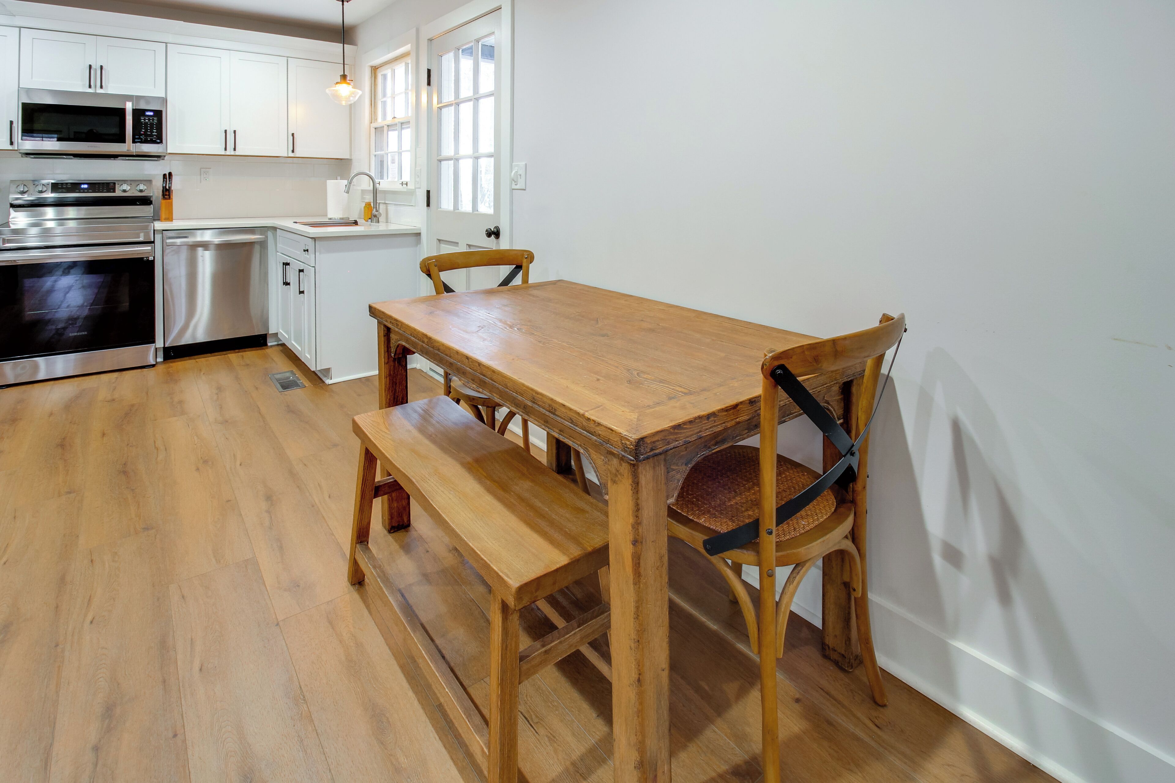 Una cocina con armarios blancos, electrodomésticos de acero inoxidable, una mesa de madera y un banco.