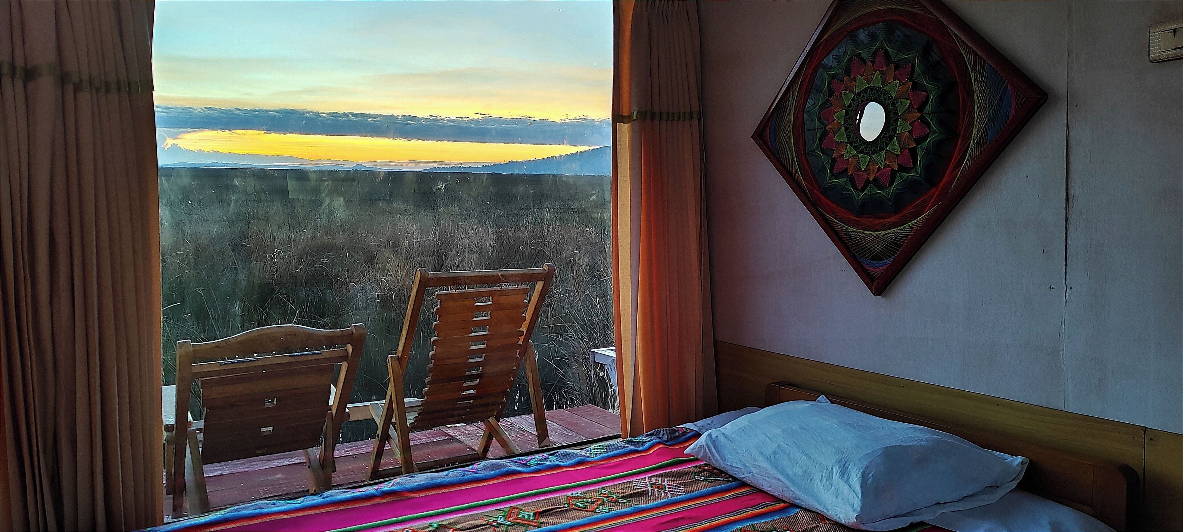 Quarto com uma cama, uma cadeira de madeira e vista para uma paisagem pela janela.