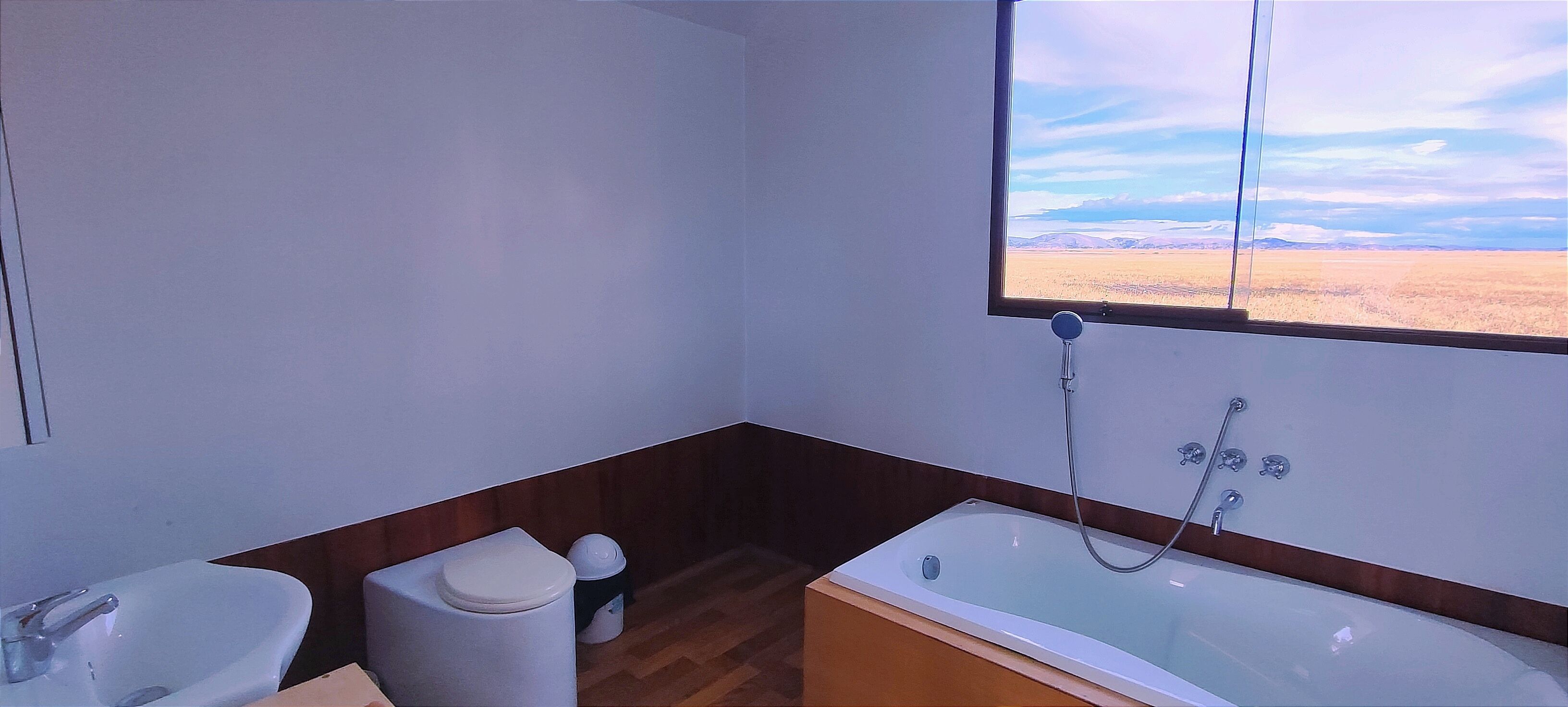 A bathroom with a bathtub, toilet, sink, and a window with a view of a desert landscape.
