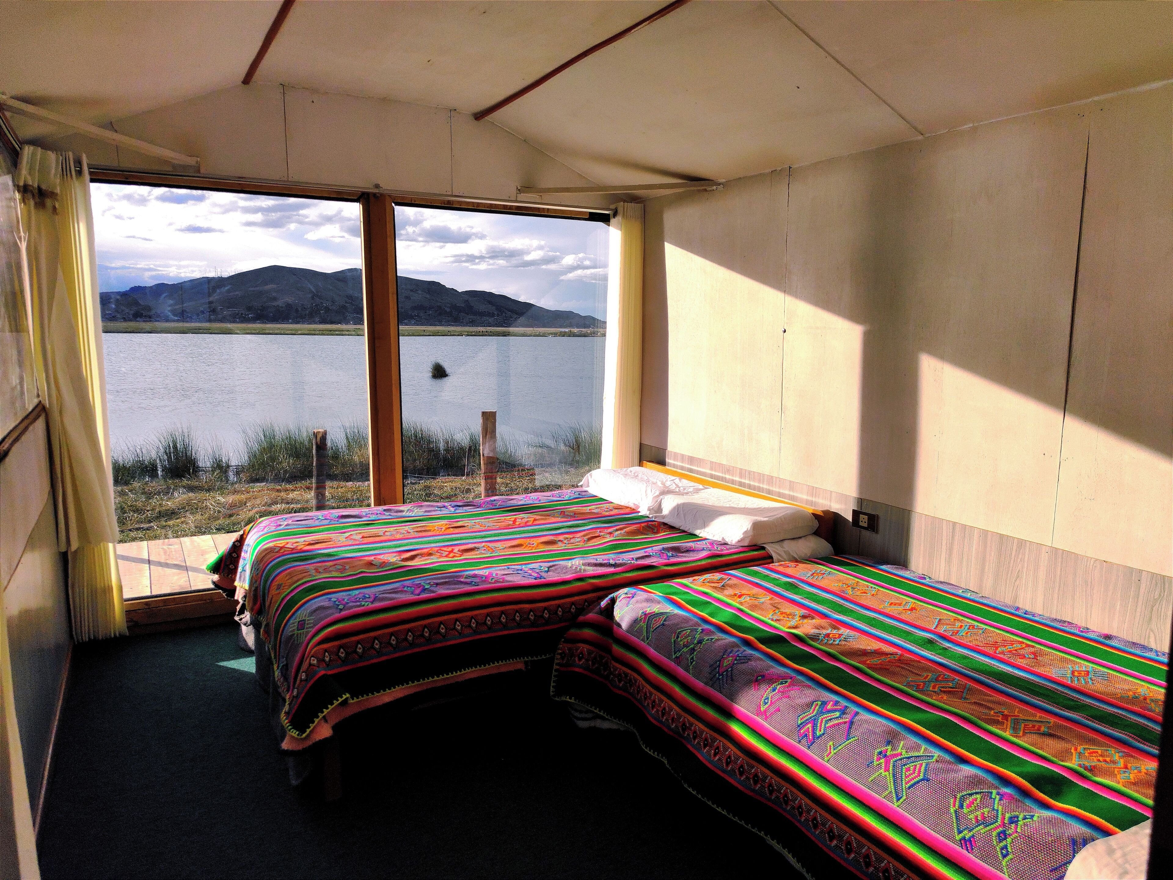 A room with two beds, a large window, and a view of a lake and mountains.