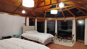 A bedroom with two beds, a wooden ceiling, and a view of the city at night. - Vanalux Titicaca (Puno)
