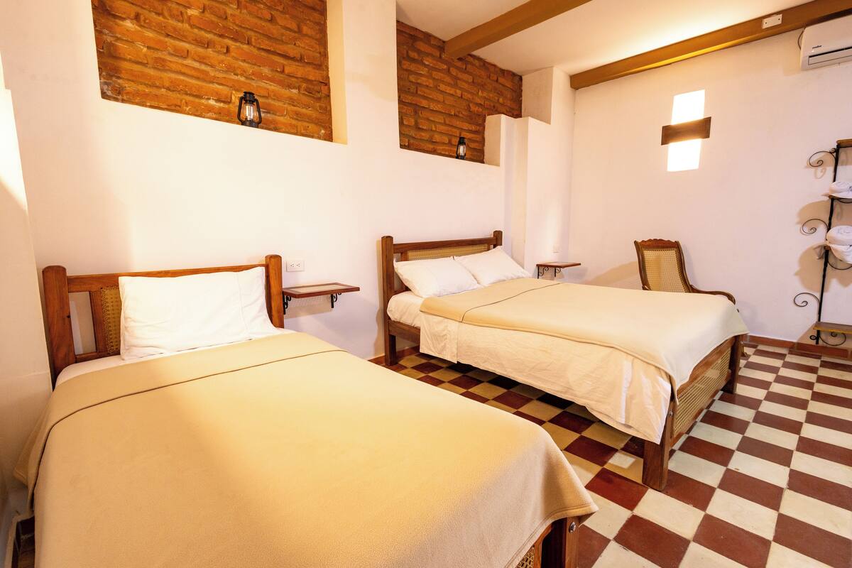 A room with two wooden beds, a checkered floor, a brick wall, and a hanging towel rack.