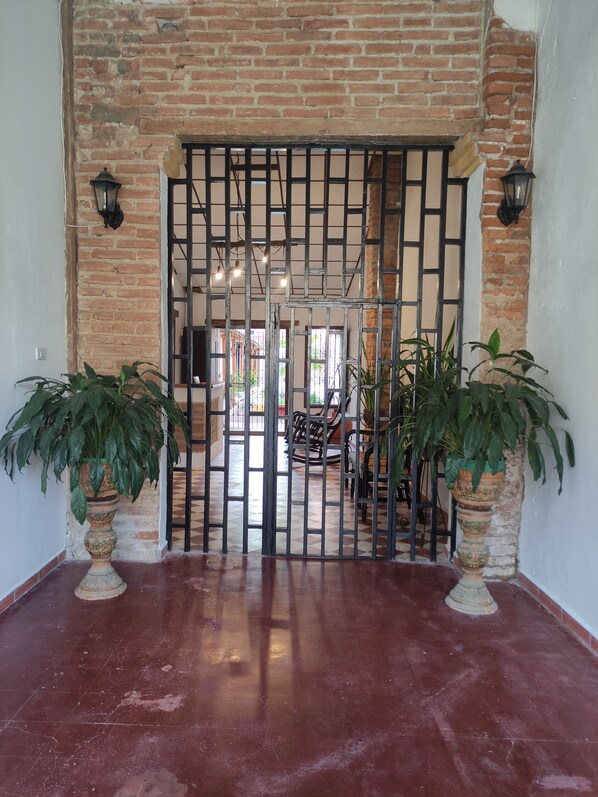 Un muro de ladrillo con una reja de metal, plantas en macetas y un piso de baldosas.