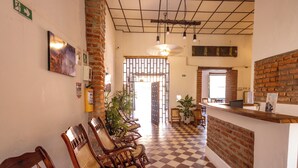 Un área de recepción con piso a cuadros, sillas de madera, un mostrador de recepción y una pared de ladrillo.