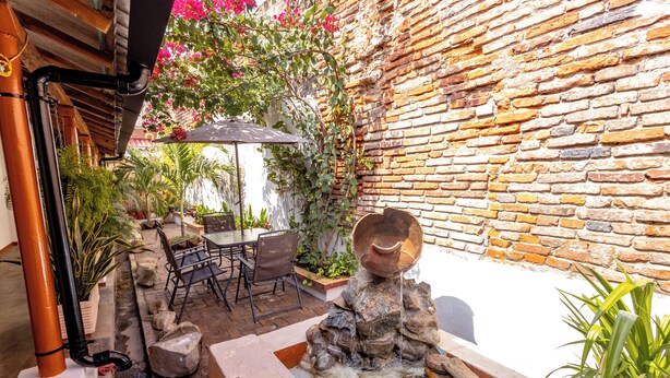 Un patio con muro de ladrillo, fuente de piedra, plantas en macetas y mobiliario exterior.
