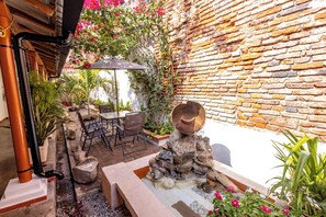 A courtyard with a brick wall, a stone water feature, potted plants, and outdoor furniture.