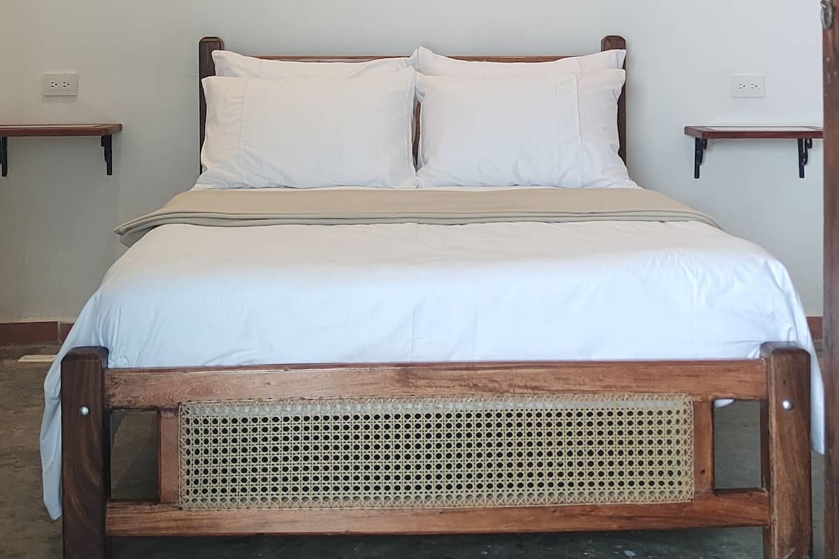 A bedroom with a wooden bed, two bedside tables, a ceiling fan, and two hanging lamps.
