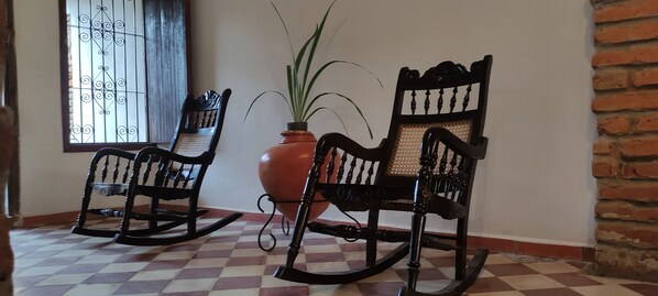 Two rocking chairs, a potted plant, and a window with a metal grille.