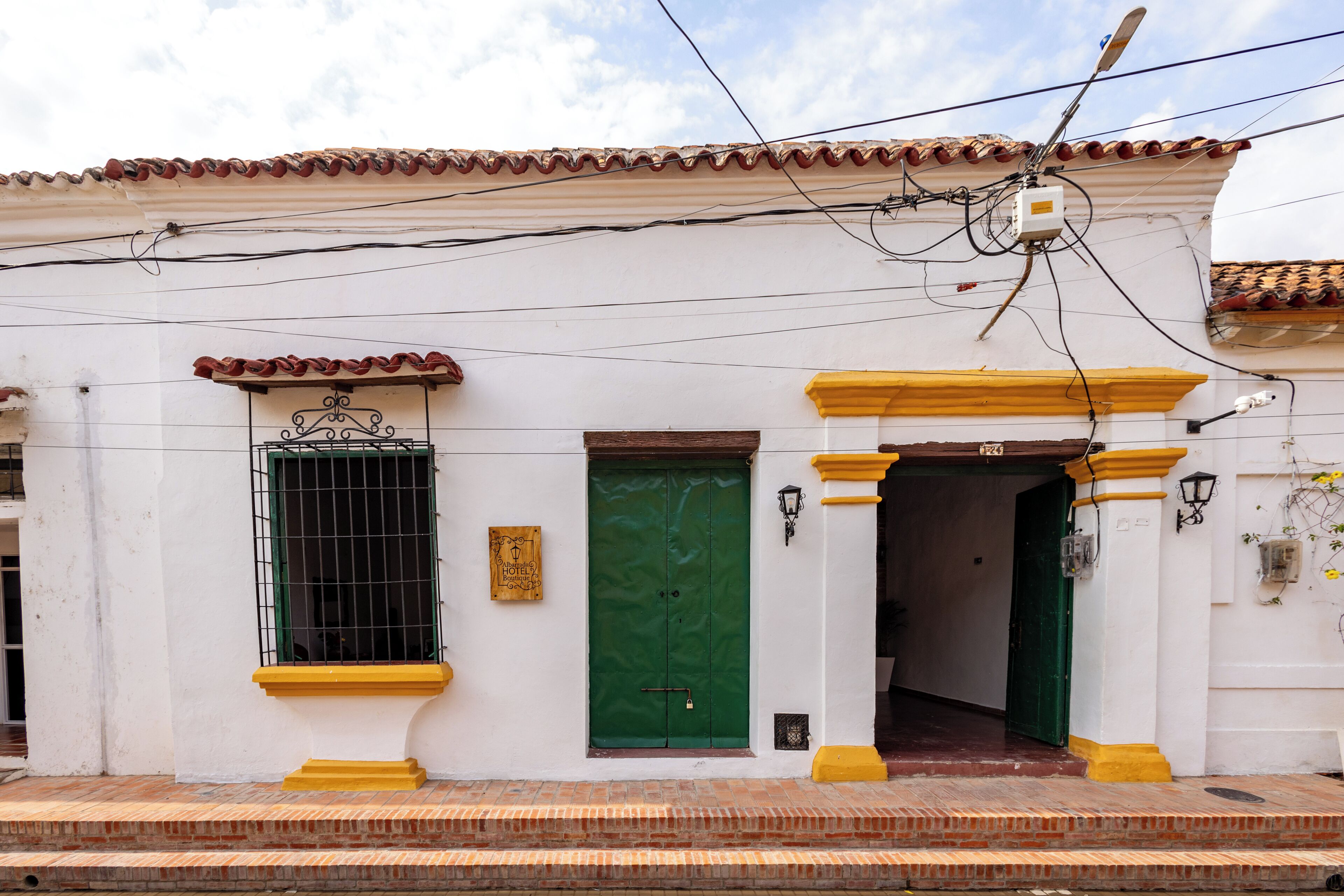 Un edificio blanco con puerta verde y detalles amarillos, que presenta un tejado de tejas y cableado eléctrico visible.