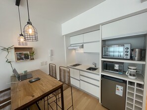 Une cuisine moderne avec des armoires blanches, un four à micro-ondes encastré, une machine à café et un réfrigérateur. On y trouve une table à manger en bois, des chaises et un ordinateur portable posé dessus.
