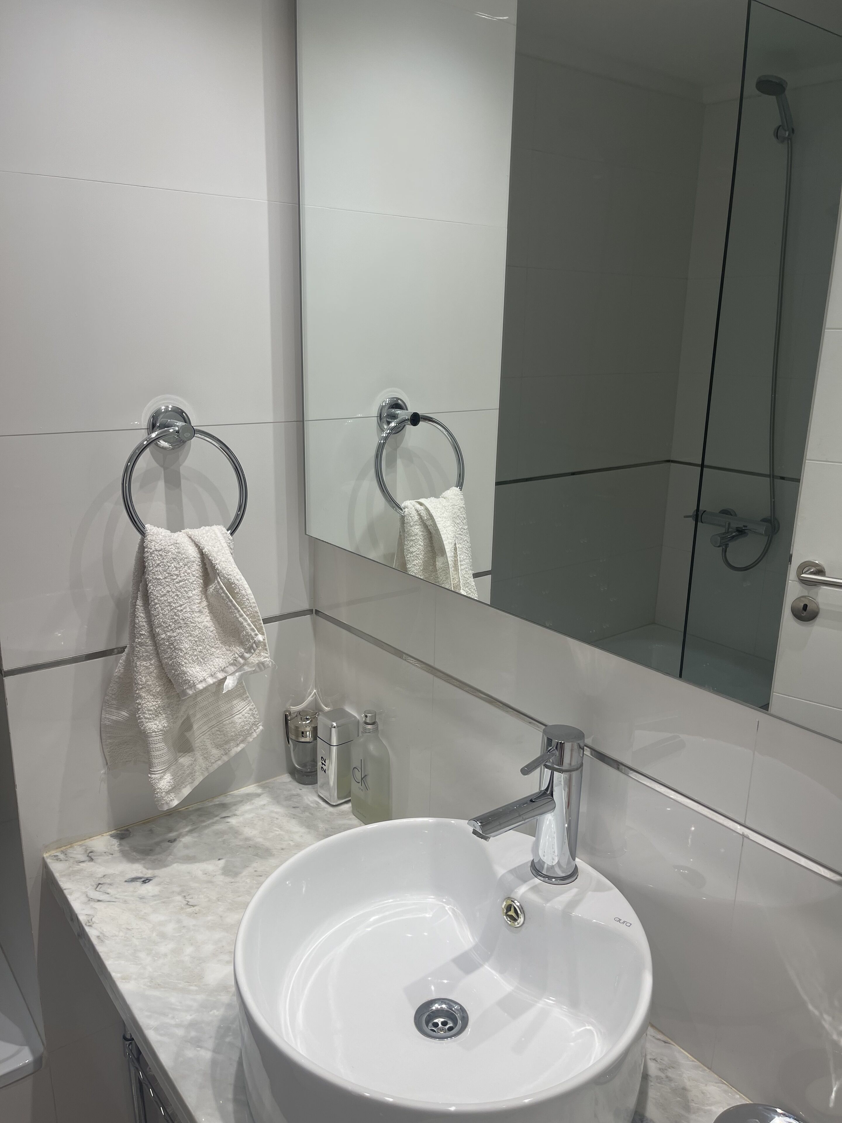 A modern bathroom with a white sink, chrome fixtures, and a large mirror reflecting the shower area.
