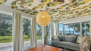 Quarto com mesa de jantar, cadeiras, sofá e uma grande janela com vista para o exterior.