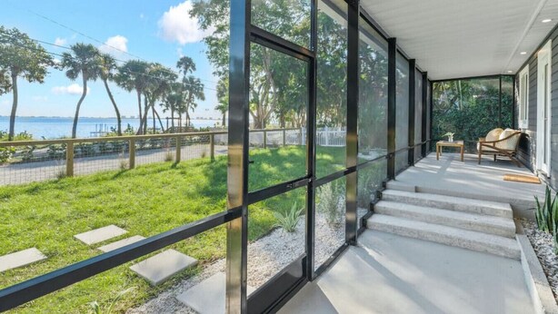 Uma casa moderna com grandes janelas de vidro, um alpendre coberto e vista para o mar.