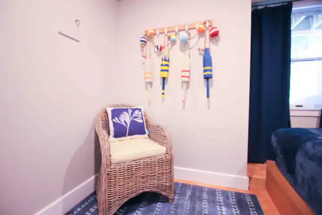 A room with a wicker chair, a wall-mounted ball rack, and a bed.