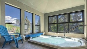 A hot tub in a room with large windows, a blue chair, and a view of trees and mountains. - Recently Renovated Ski In-Out on Purgatory Mountain (Durango)